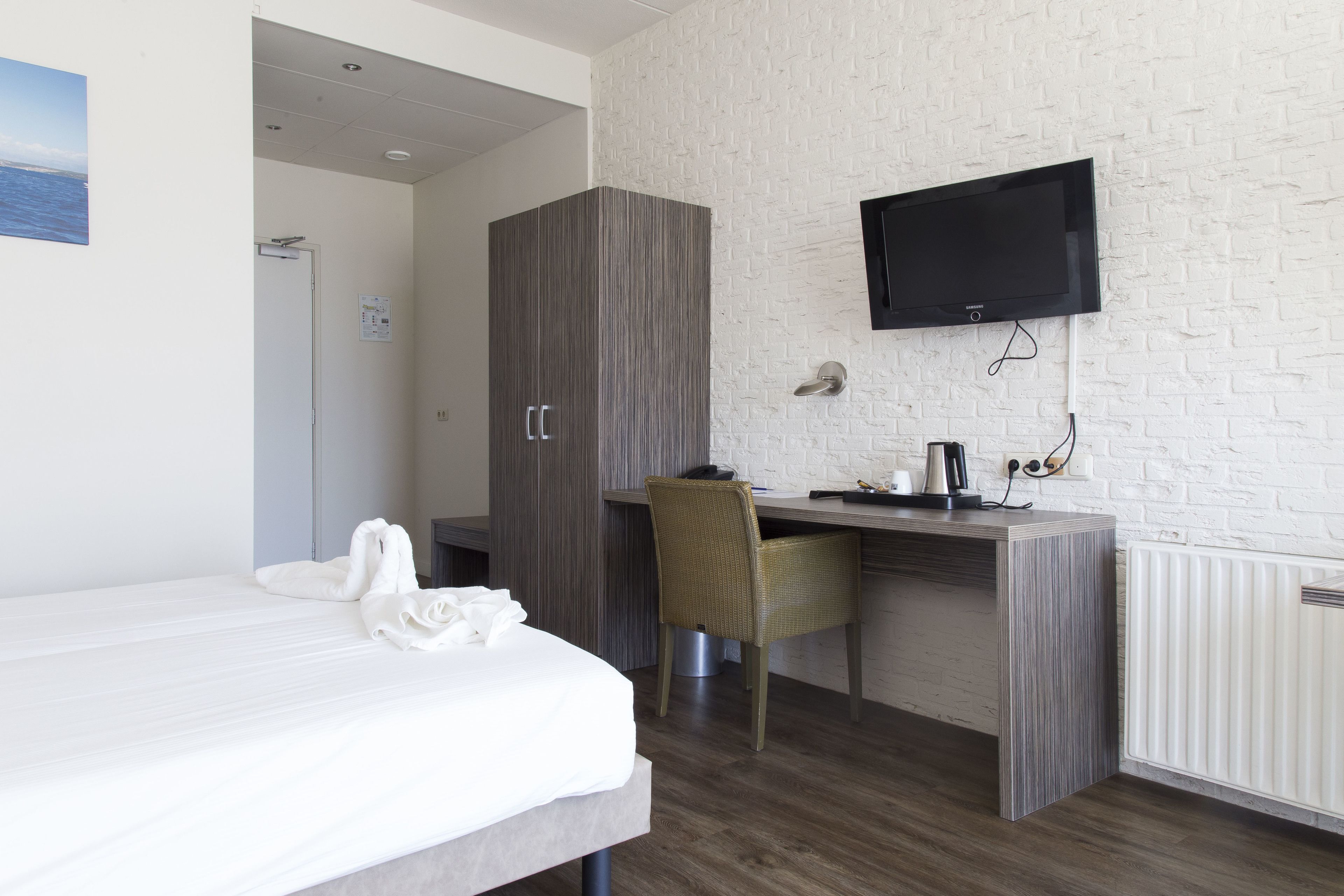 Una habitación de hotel con cama, escritorio, silla, televisor y armario.