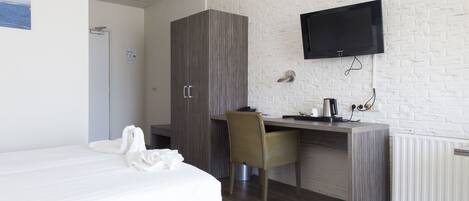 A hotel room with a bed, a desk, a chair, a television, and a wardrobe.