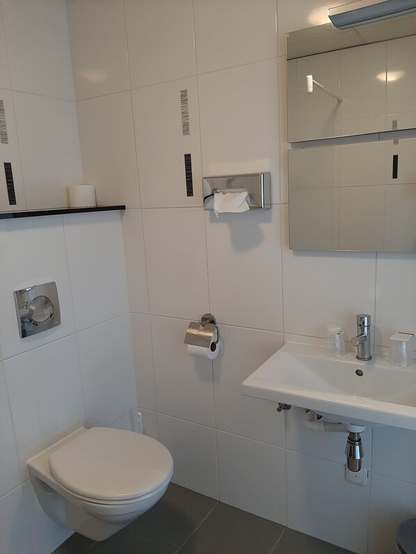 A modern bathroom with a toilet, a sink, a mirror, and a paper towel dispenser.