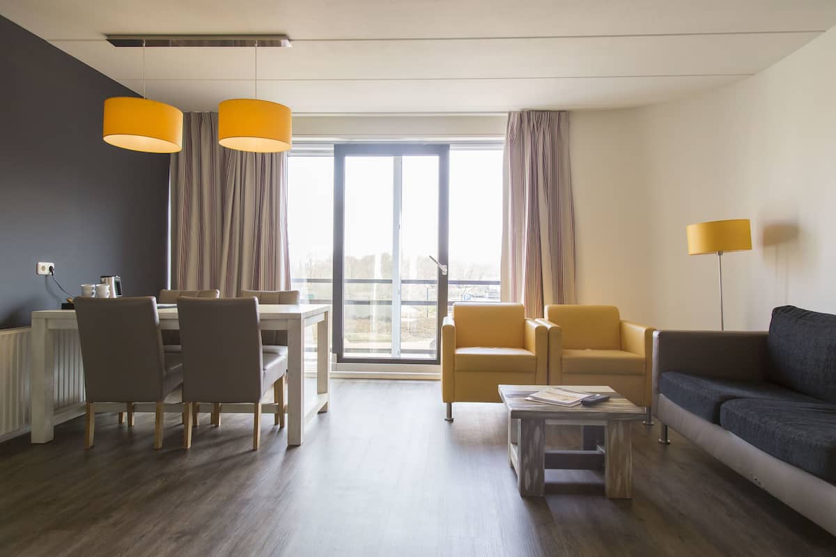 Una sala de estar moderna con comedor, que incluye un sofá, sillas, una mesa de centro y vistas a través de un ventanal.