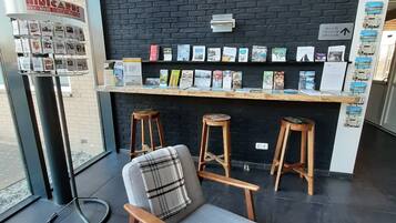 Un interior moderno con una pared de ladrillo negro, una encimera de madera con libros y una zona de estar con un sillón gris y taburetes de madera.