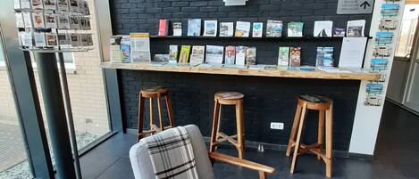 Un interior moderno con una pared de ladrillo negro, una encimera de madera con libros y una zona de estar con un sillón gris y taburetes de madera.
