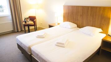 Een hotelkamer met twee bedden, een klein tafeltje met een stoel, een lamp en een nachtkastje met een telefoon.