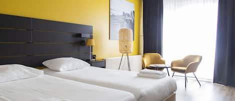 Une chambre d’hôtel avec deux lits, une grande fenêtre avec des rideaux, une chaise, une lampe et un tableau au mur.