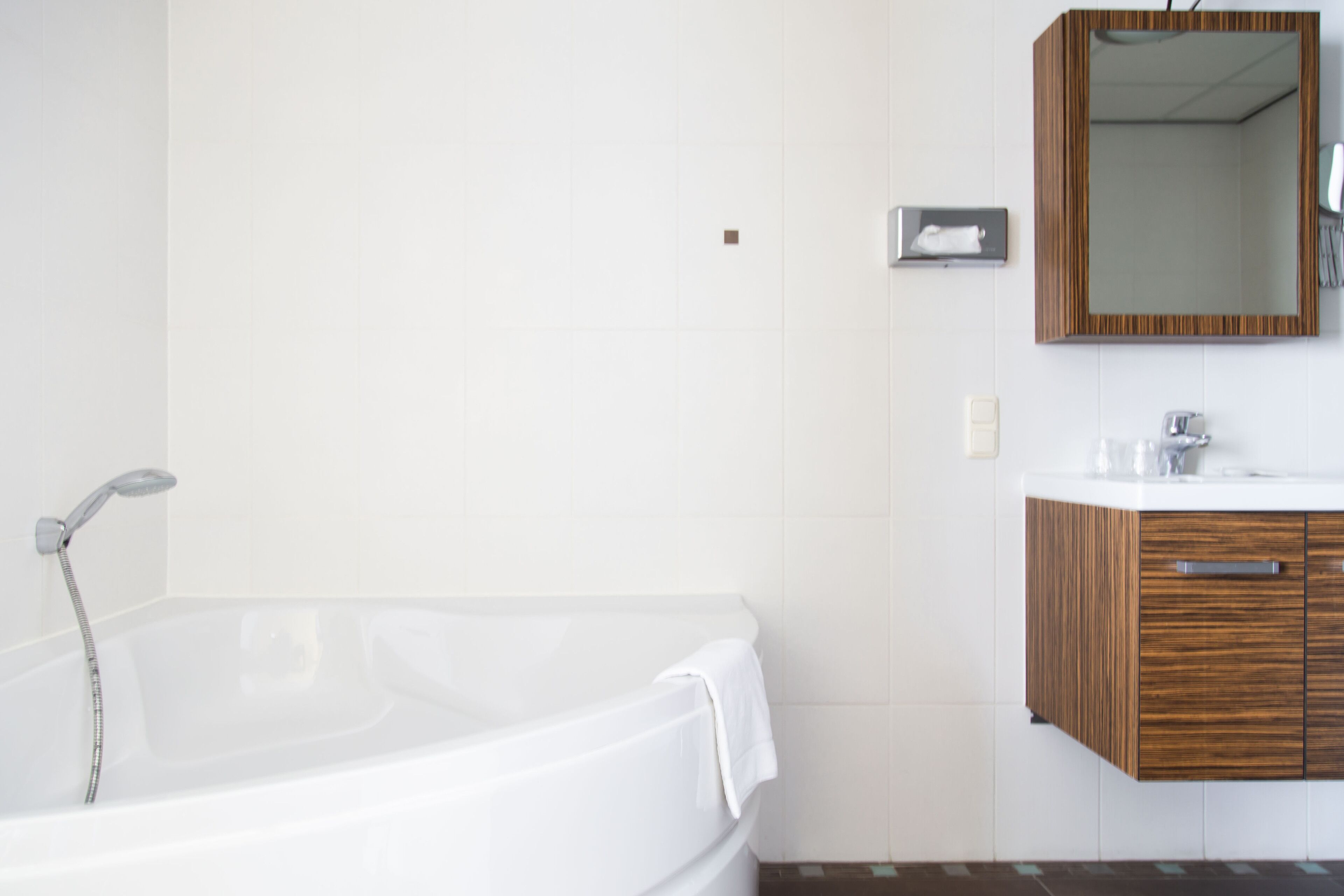 A modern bathroom with a white bathtub, wooden vanity, and a mirror.