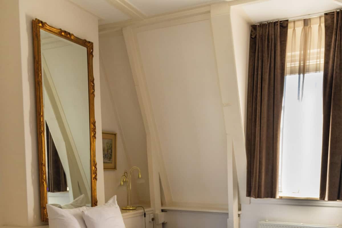 Un dormitorio con dos camas, un espejo grande, una mesita de noche, una lámpara y un ventanal con cortinas.