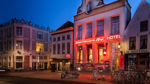 Un hotel de estilo arquitectónico europeo clásico, con una torre del reloj destacada y un letrero de neón rojo.