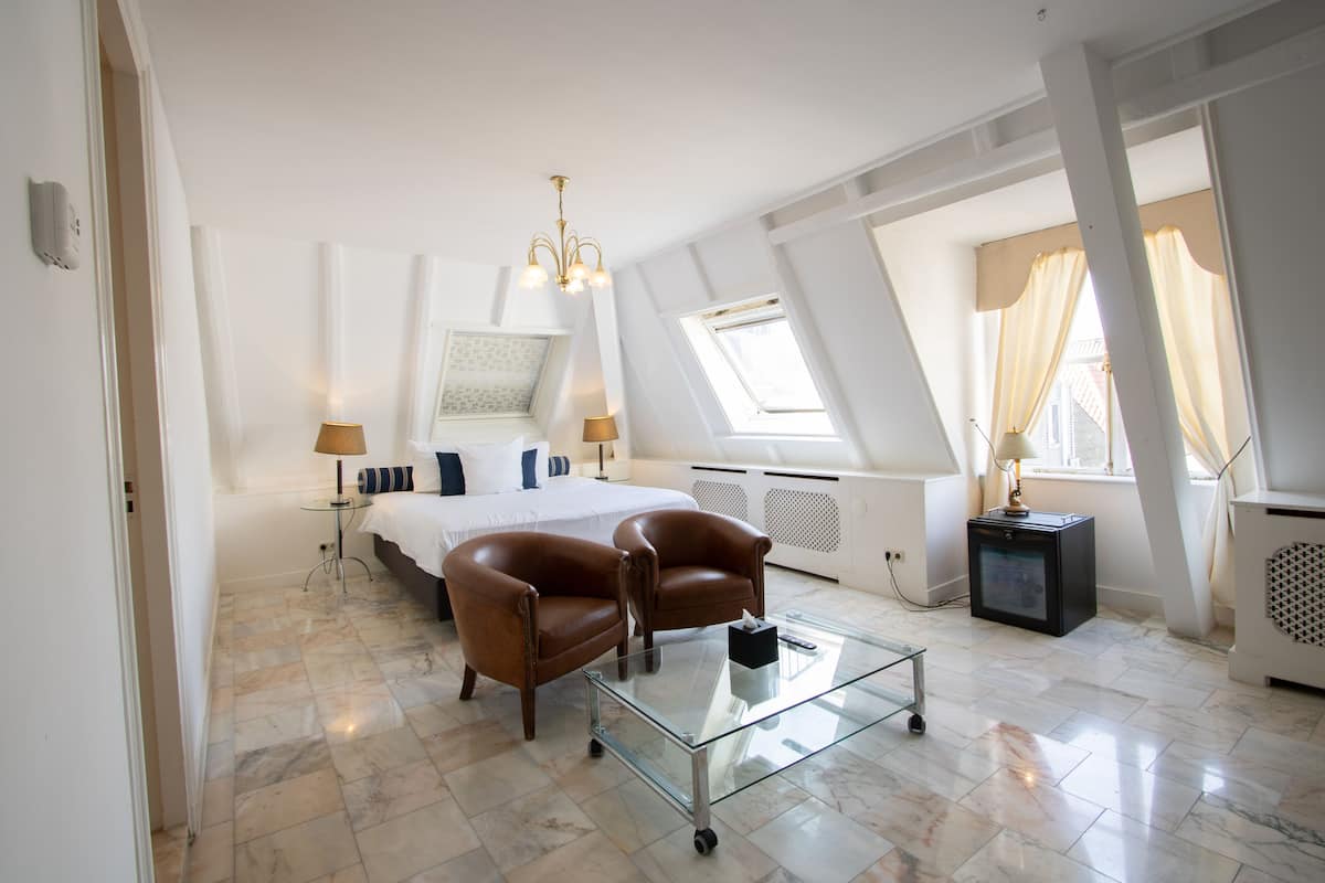 Un dormitorio moderno con una cama grande, dos sillones de cuero, una mesa de centro de vidrio y una lámpara en el techo.