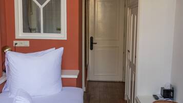 A hotel room with a bed, a wooden floor, a white wardrobe, a small wooden table, and a door leading to another room.