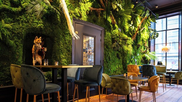 Un restaurante con pared verde, mesas y sillas de madera.