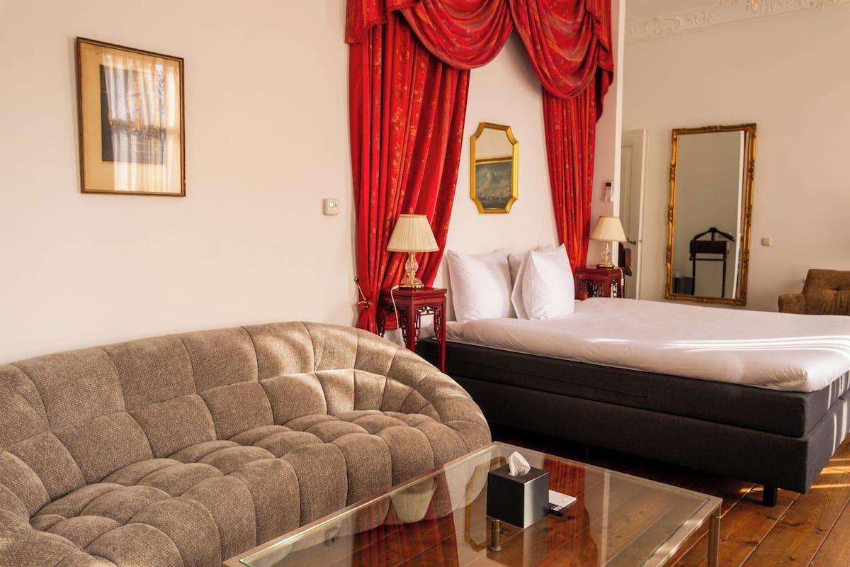 Un dormitorio con una cama, un sofá, una mesa de centro de vidrio y cortinas rojas.
