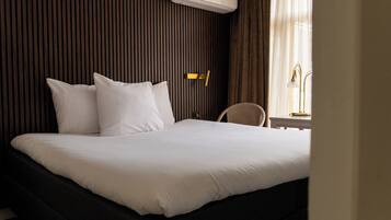 Une chambre d’hôtel avec un grand lit, une table de chevet, une chaise et une fenêtre avec des rideaux.