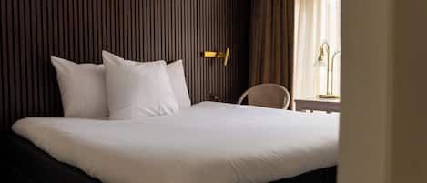 Habitación de hotel con una cama grande, una mesita de noche, una silla y un ventanal con cortinas.