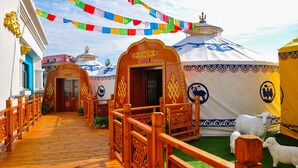 A corridor with wooden railings leading to yurts, decorated with colorful prayer flags. - Country Garden Phoenix Hotel Tongliao (Tongliao)
