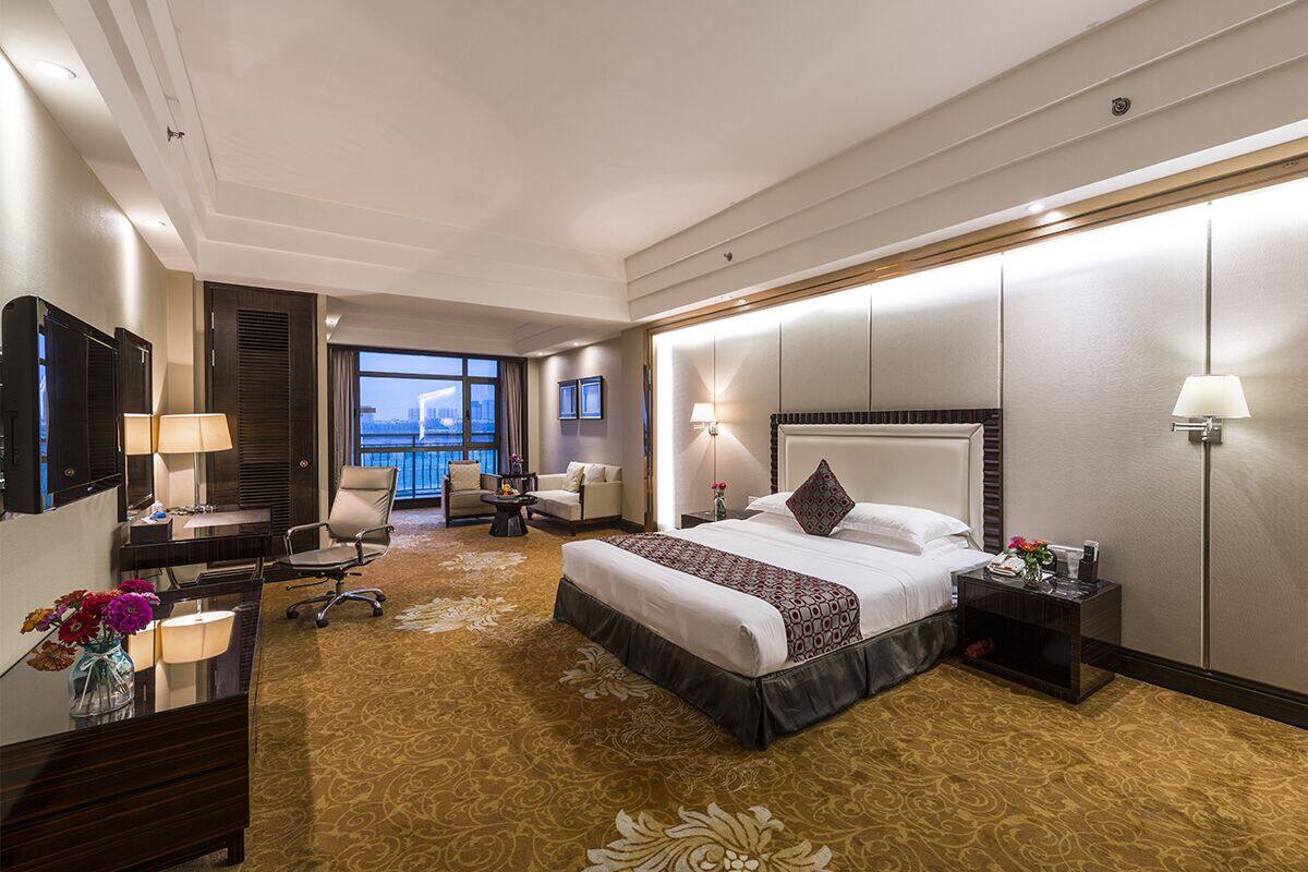 Ein Hotelzimmer mit einem großen Bett, einem Schreibtisch, einem Stuhl, einem Fernseher und Blick auf die Stadt.