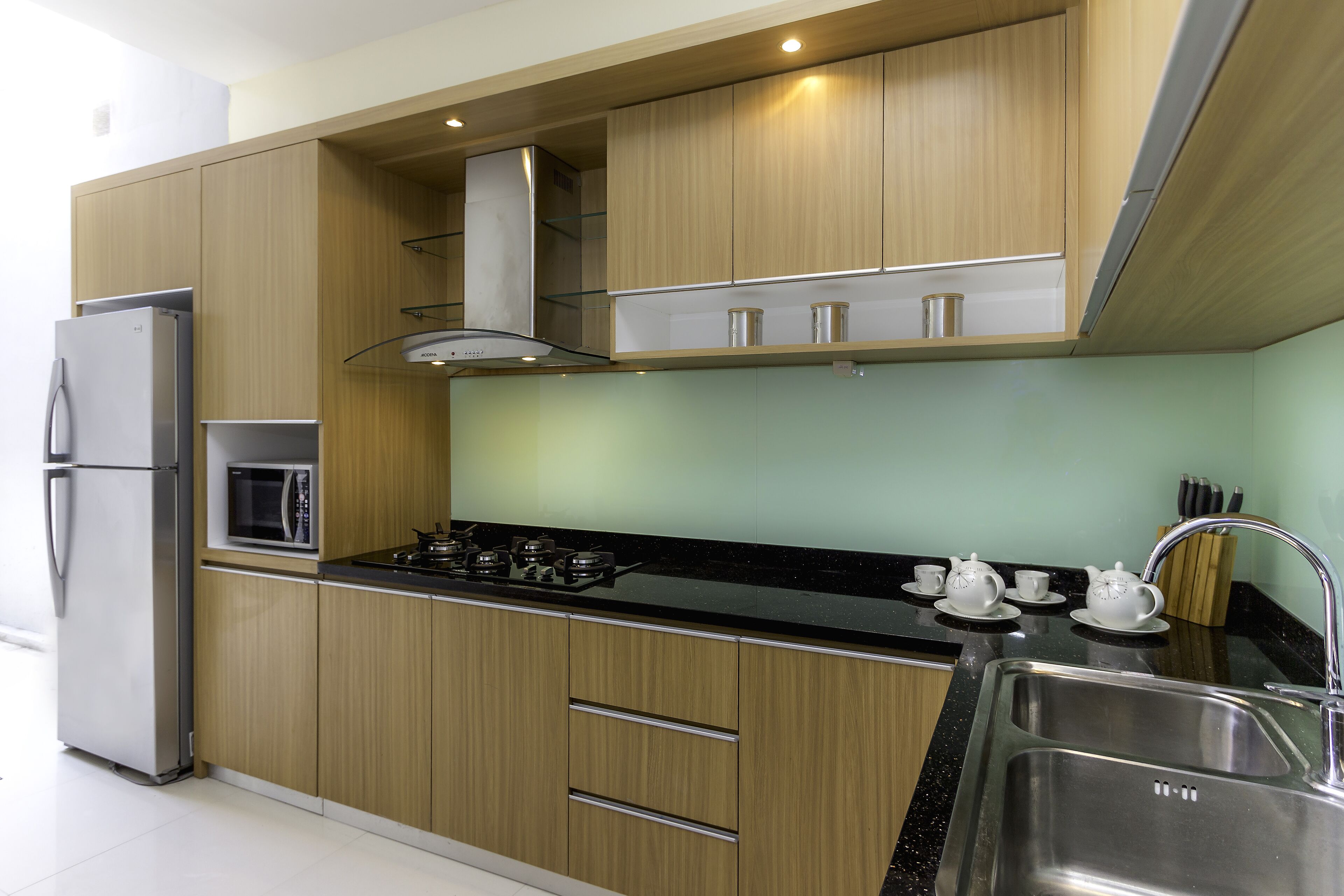 Eine moderne Küche mit Holzausstattung, einem Edelstahlkühlschrank, einer Mikrowelle, einem Gasherd und einem Spülbecken.