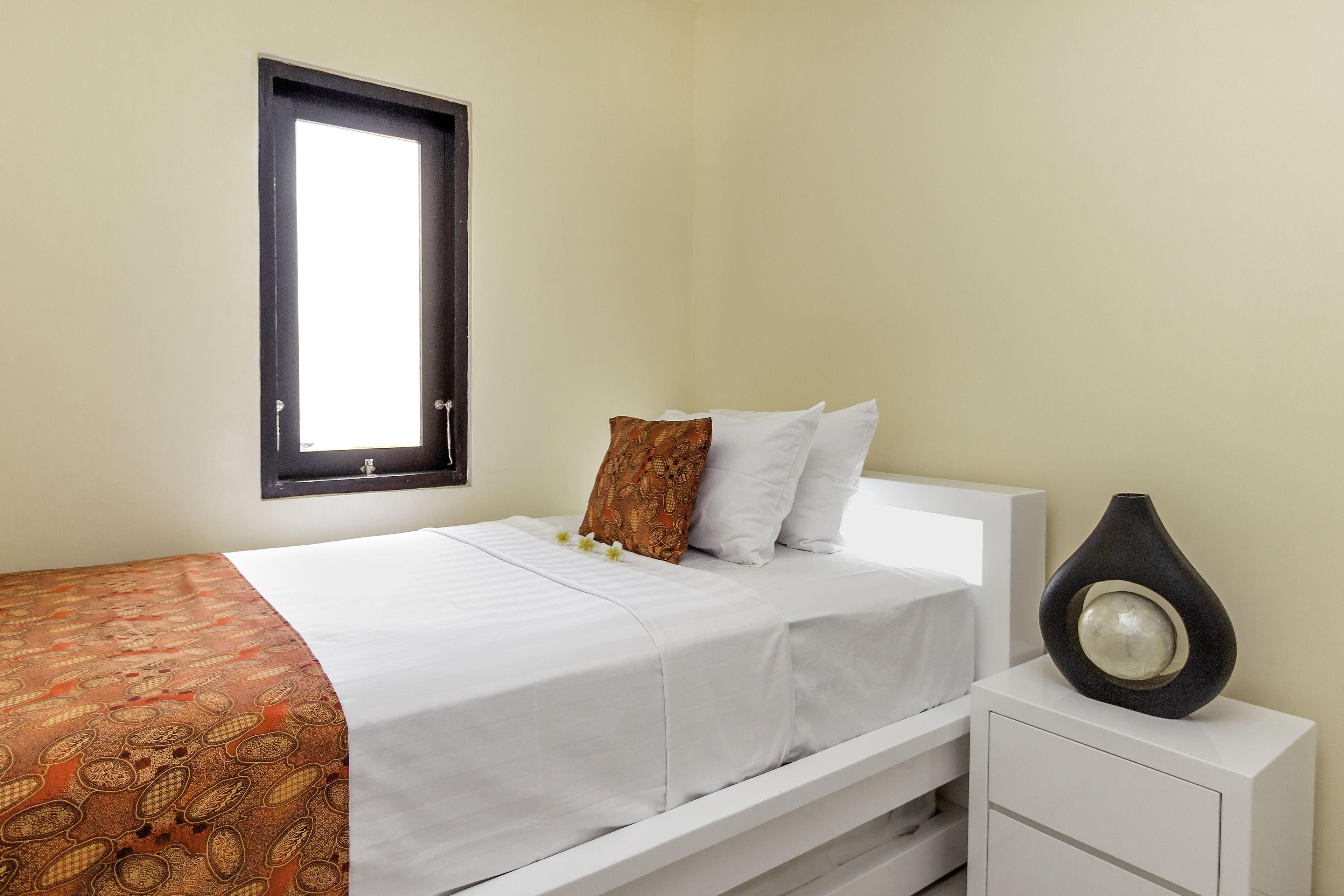 Una cama bien hecha con una colcha estampada, almohadas blancas y un jarrón decorativo sobre una mesita de noche.