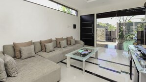 Una sala de estar moderna con un sofá seccional, una mesa de centro de vidrio y un ventanal corredero que da a un espacio exterior.