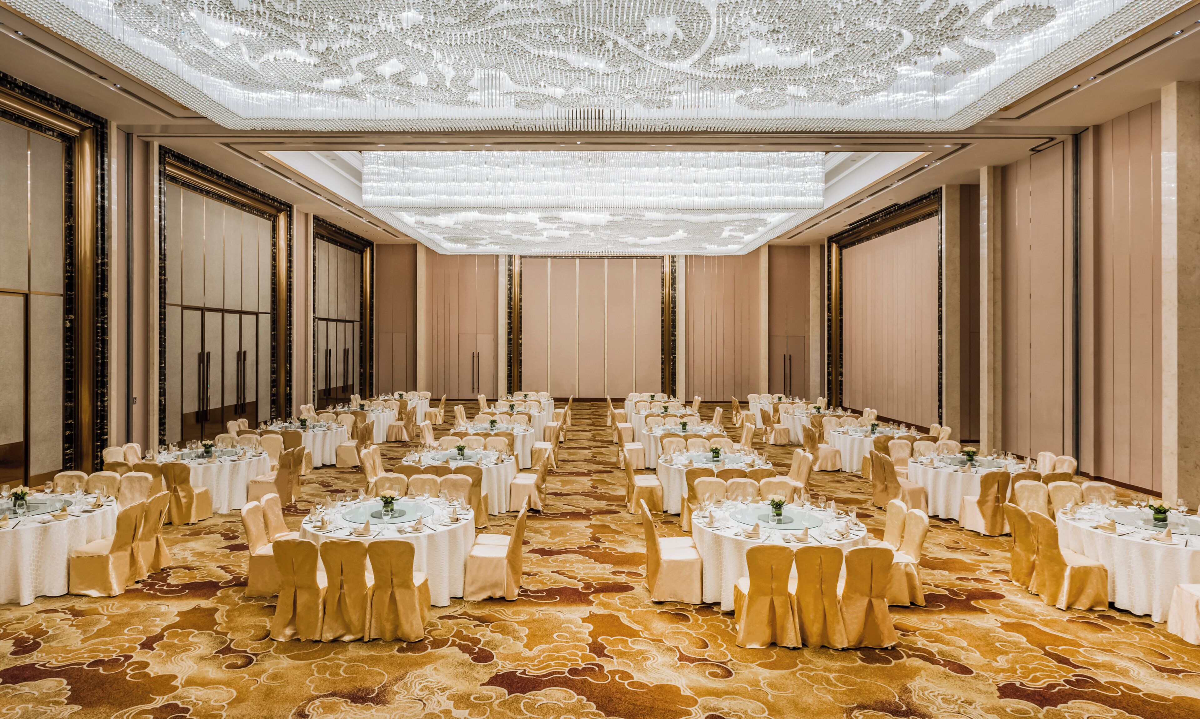 A banquet hall with round tables, chairs, and a patterned carpet.