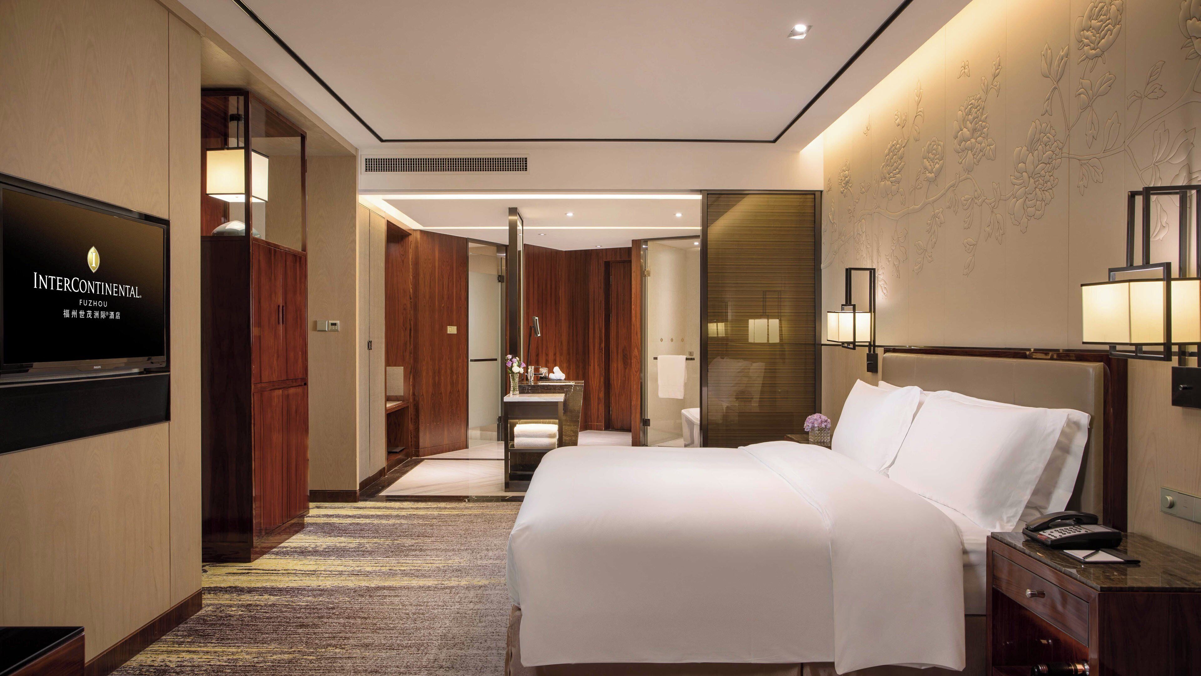 Una habitación de hotel con cama, televisión, baño y escritorio con lámpara.