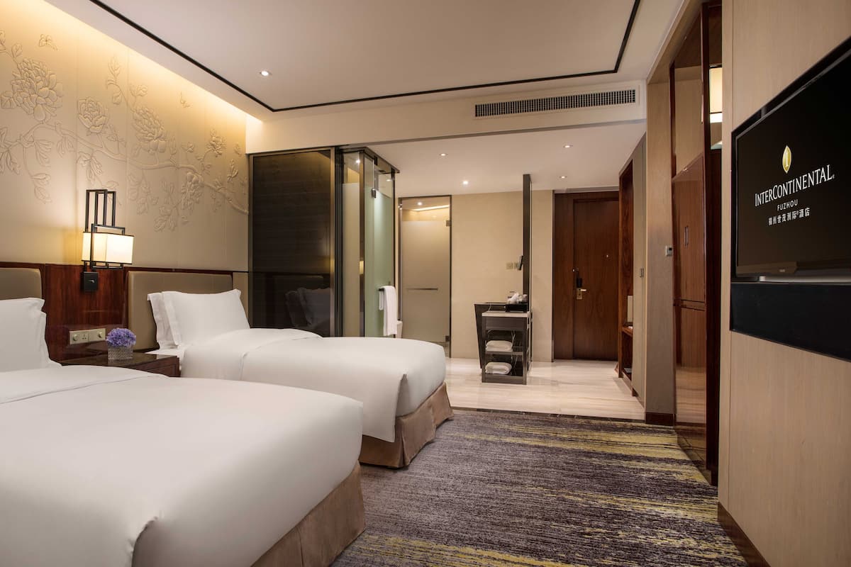 A hotel room with two beds, a large mirror, a flat-screen TV, and a carpeted floor.