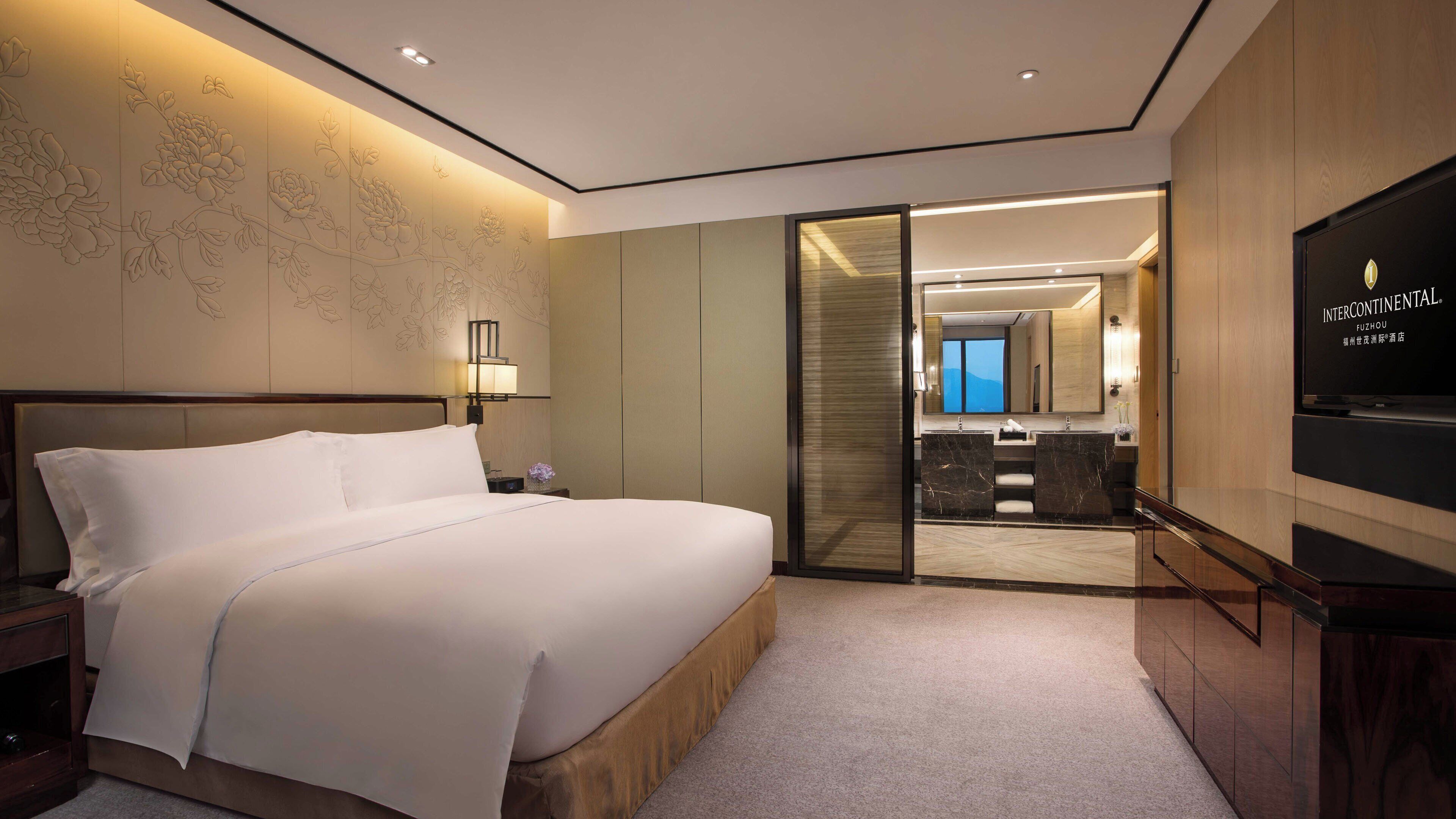 Une chambre d’hôtel dotée d’un grand lit, d’un téléviseur à écran plat, d’un bureau et d’une porte coulissante donnant accès à une salle de bain avec un lavabo et un miroir.