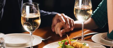 A dining table with two wine glasses, a plate of food, and a person's hands resting on the table.