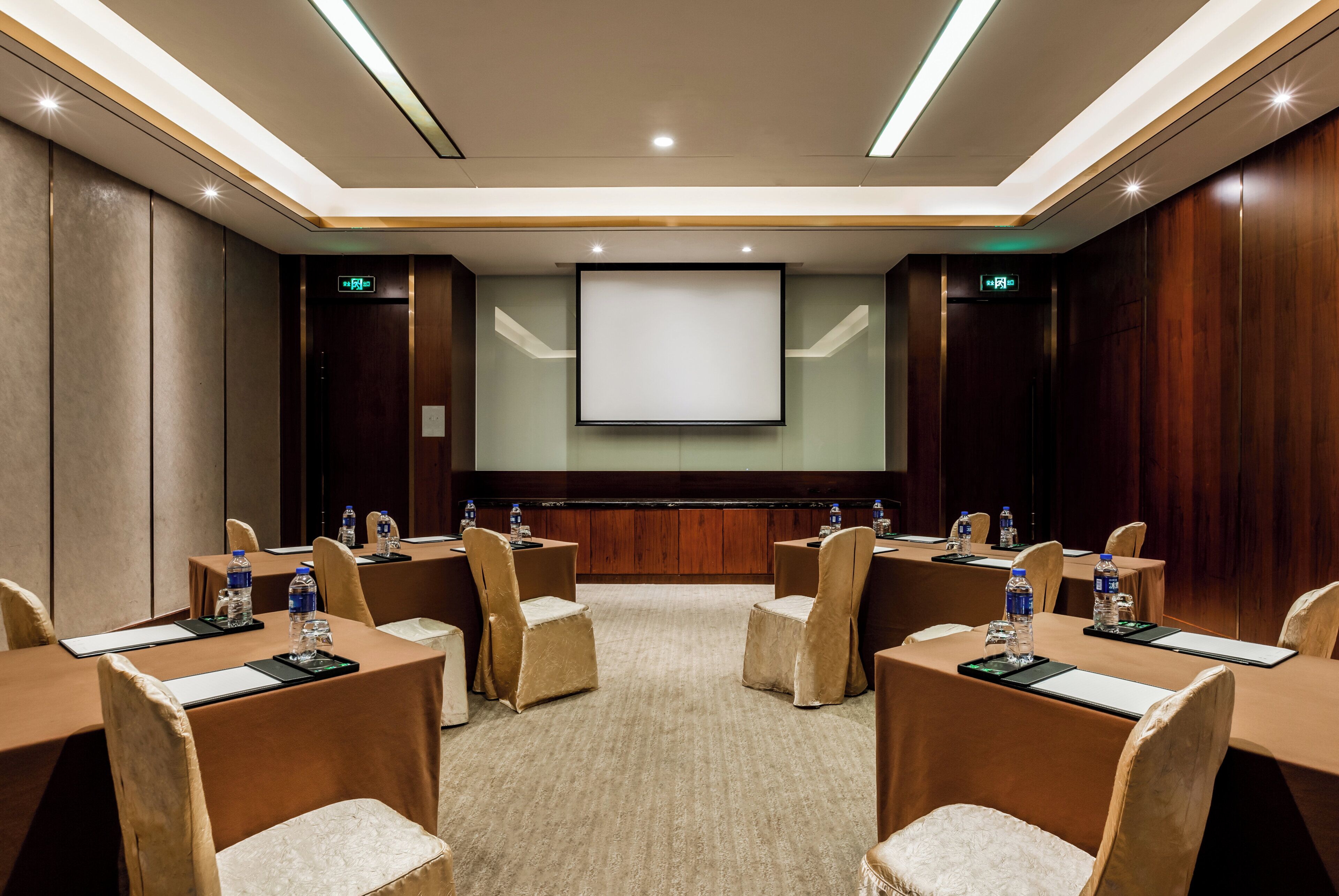 A conference room with a large screen, multiple tables with chairs, and water bottles.