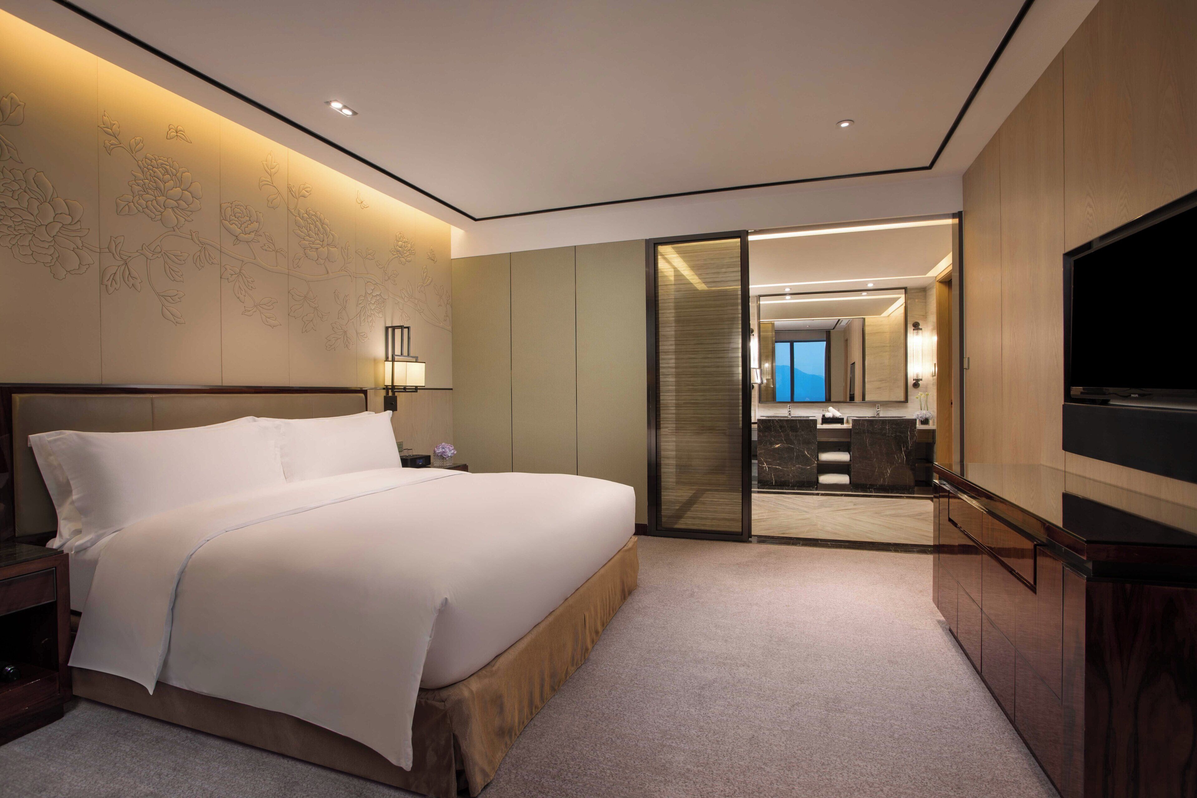 Quarto de hotel com uma cama grande, televisão, porta de correr para o banheiro e mapa na parede.