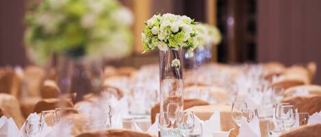 A banquet table set with white napkins, clear glassware, and a centerpiece with white flowers in a tall vase.
