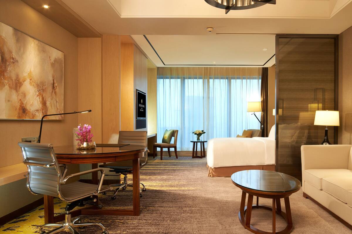 A hotel room with a bed, a sofa, a desk with a chair, a small table, and a large painting on the wall.