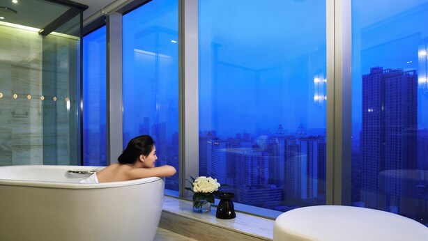 Une salle de bain moderne dotée d’une grande baignoire, d’un coin salon et offrant une vue sur le paysage urbain grâce à de larges fenêtres.