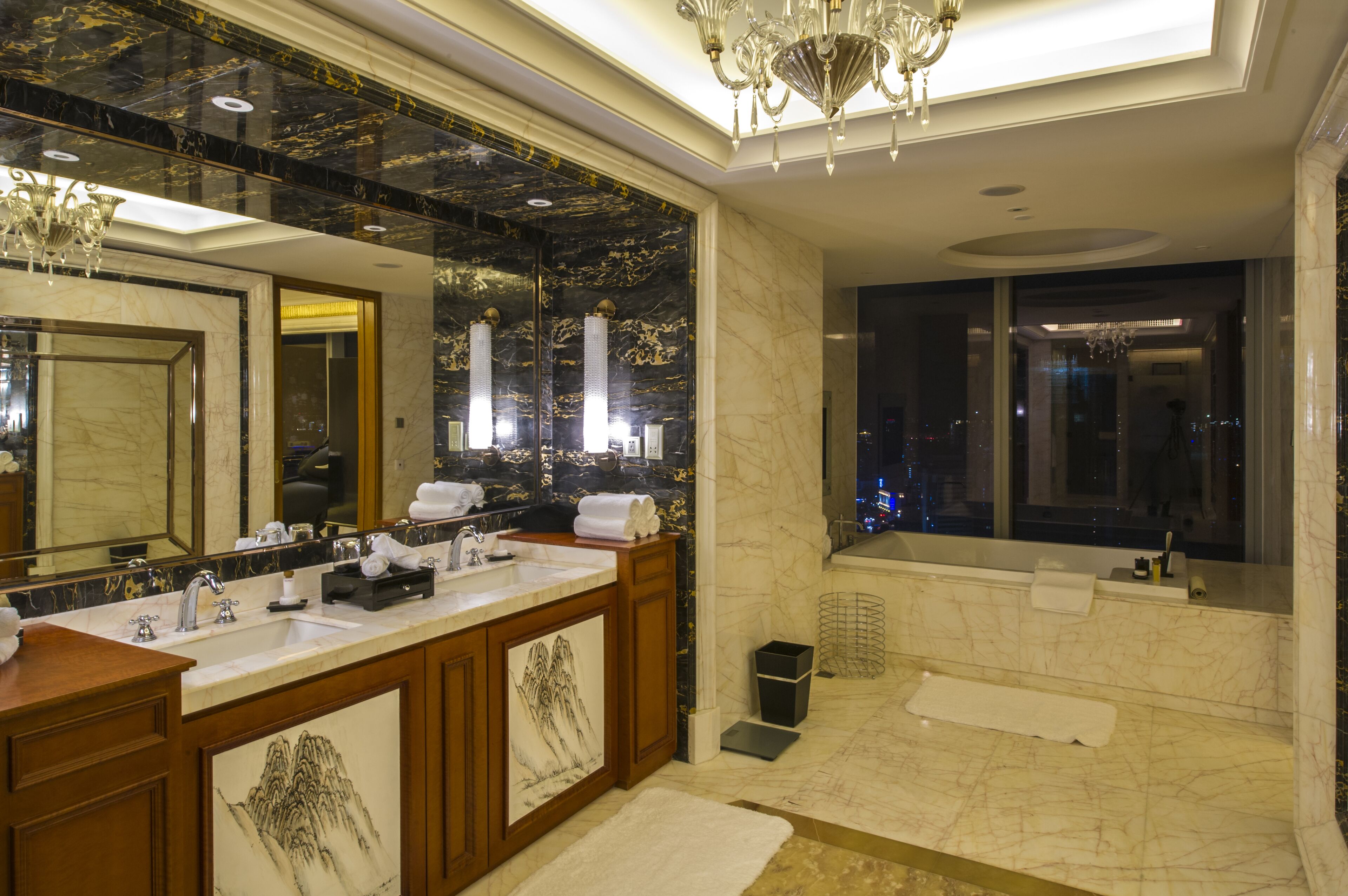 A luxurious bathroom with a large mirror, double sinks, a bathtub, and a chandelier.