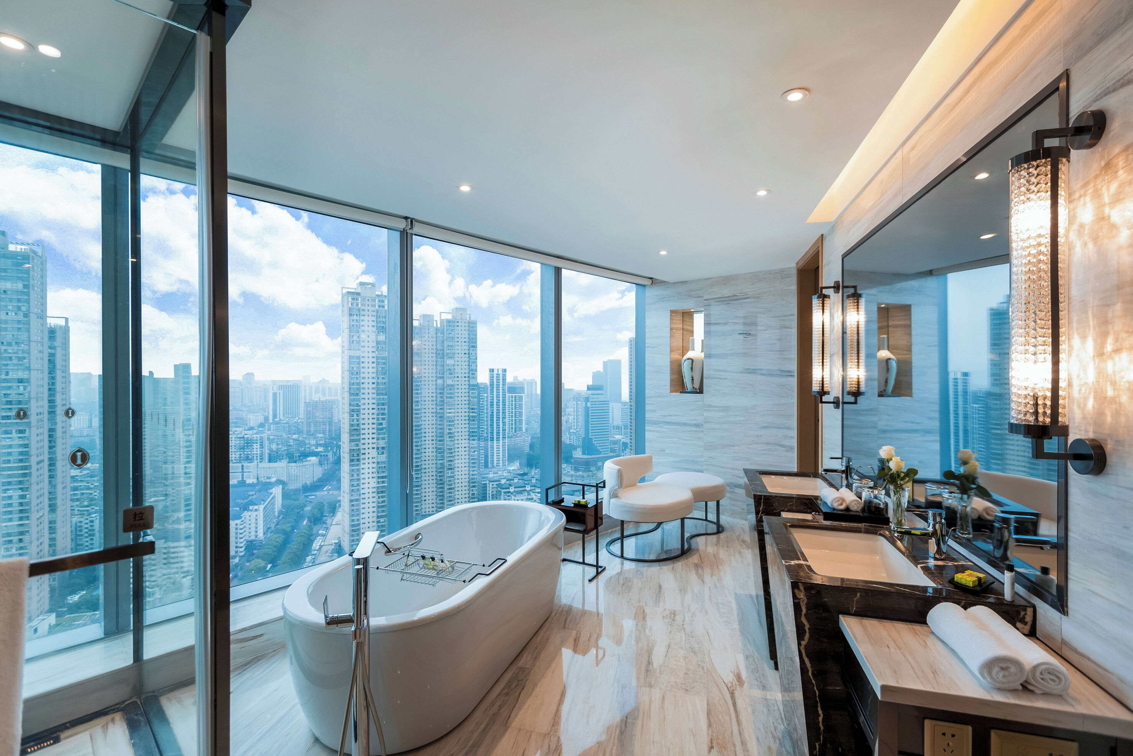 A modern bathroom with a freestanding bathtub, a vanity with a mirror, and a large window offering a city view.