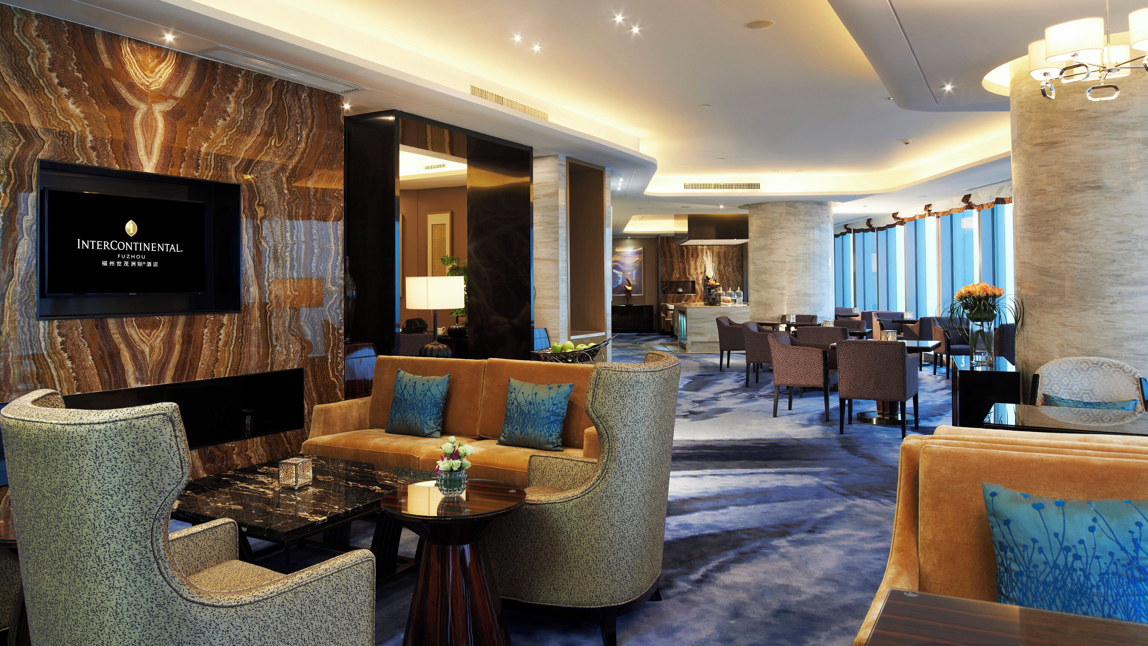 A hotel lobby with seating areas, a reception desk, and a television screen.