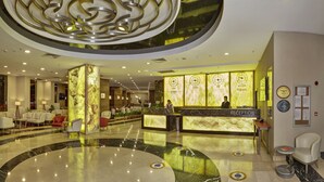 Un vestíbulo de hotel con mostrador de recepción, zona de estar y un amplio suelo de mármol.