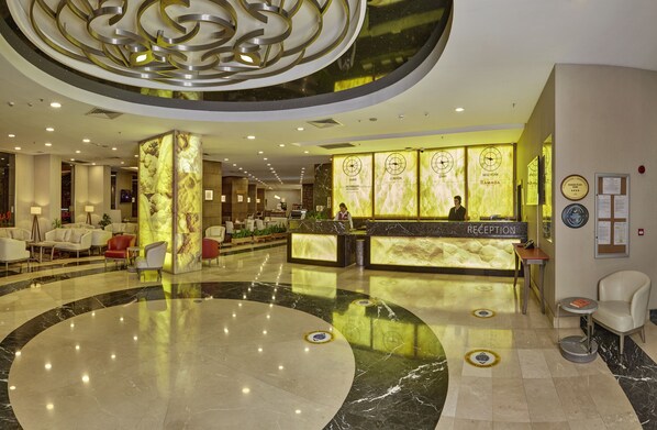 A hotel lobby with a reception desk, seating area, and a large marble floor.