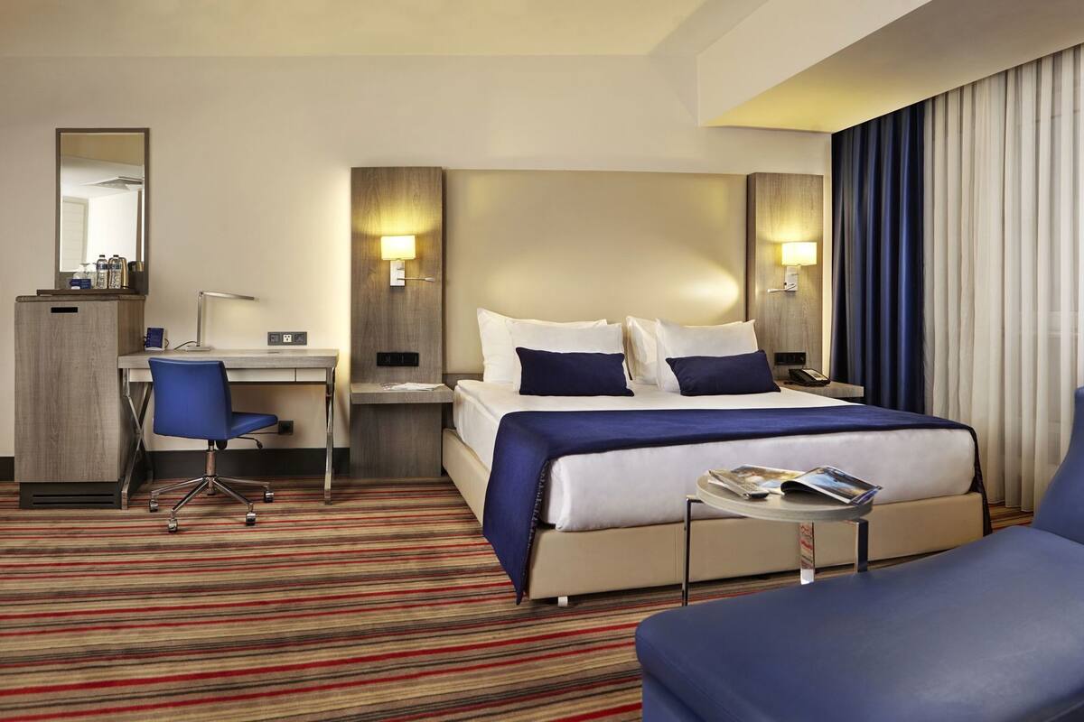 Habitación de hotel con cama, escritorio, silla y una pequeña mesa con una revista.