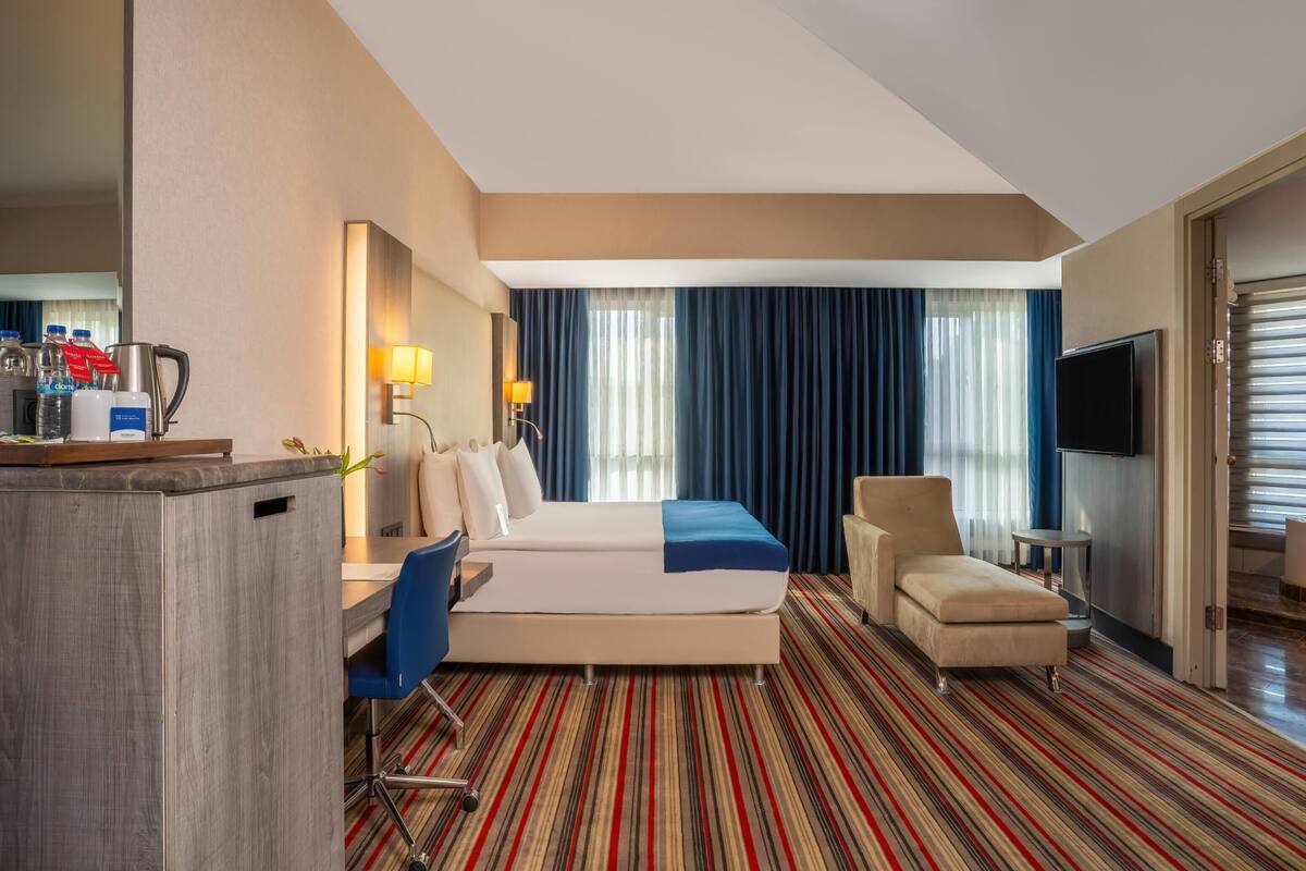 Een hotelkamer met een bed, een bureau, een stoel, een televisie en een minibar.