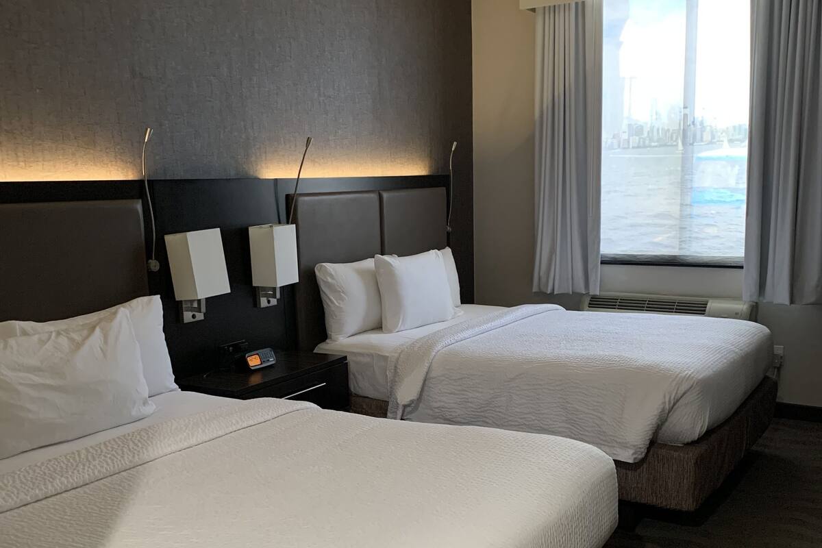 Une chambre d’hôtel avec deux lits, une table de chevet, une lampe fixée au mur et une fenêtre avec des rideaux.