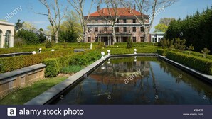 A historic building with a red roof, surrounded by a formal garden and a reflecting pool.