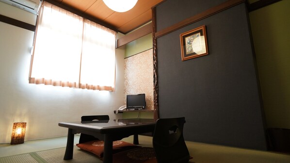 Une pièce de style japonais traditionnel, avec un sol recouvert de tatamis, une table basse, une chaise, un bureau avec un ordinateur et un tableau encadré accroché au mur.