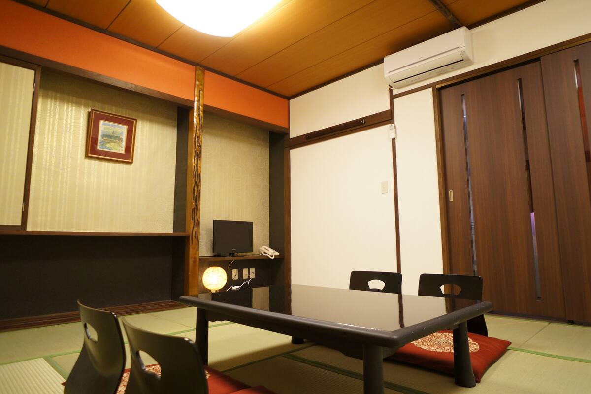 Ett traditionellt japanskt rum med tatamimattor på golvet, ett lågt bord med stolar, en tv och en skjutdörr.