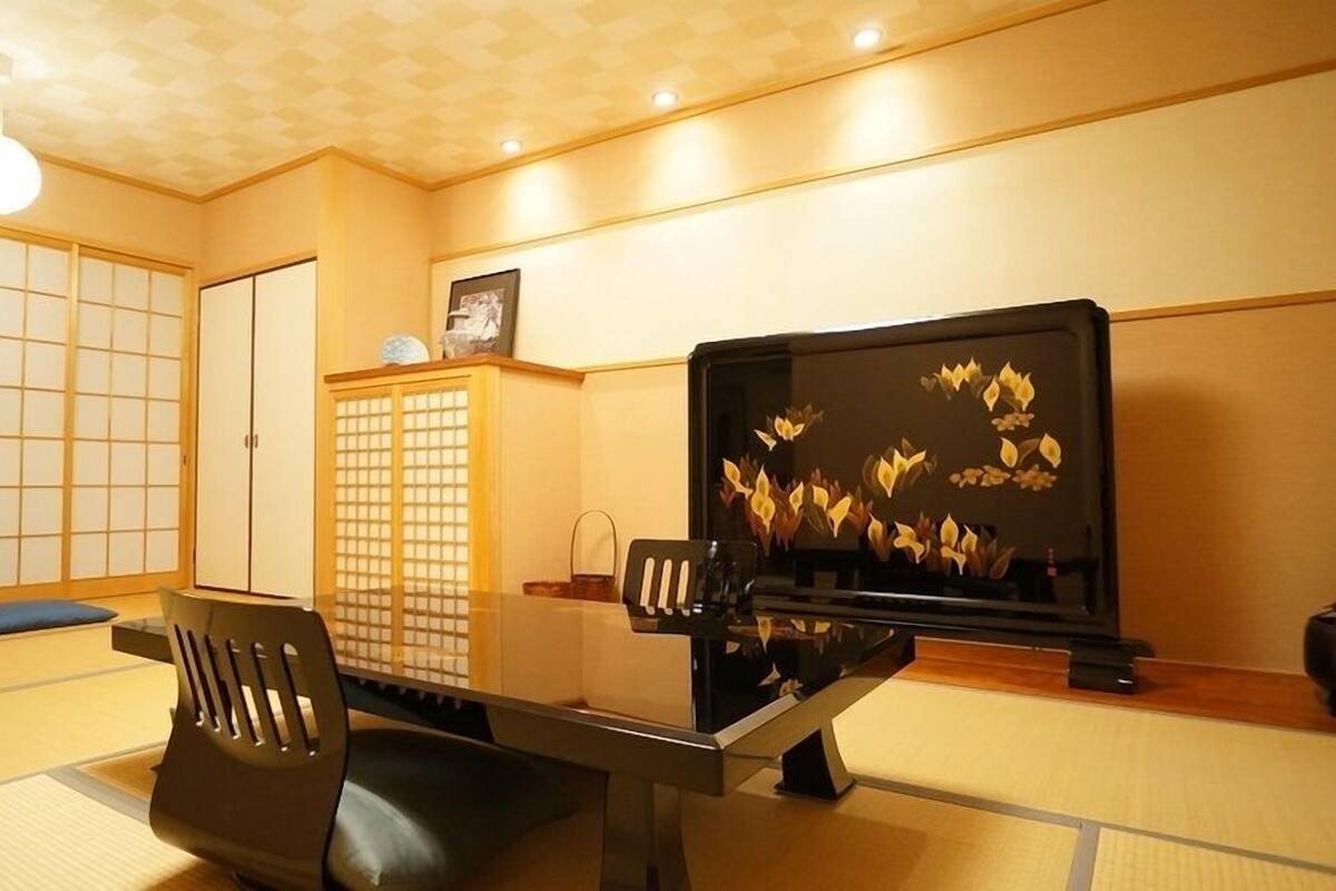 Ett traditionellt japanskt rum med tatamimattor på golvet, ett lågt bord, en svart stol, en tv och skjutdörrar.