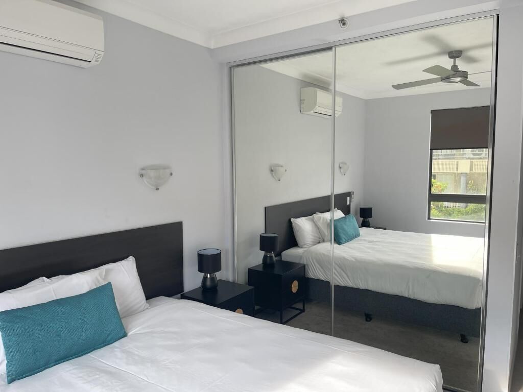 Una moderna camera d'albergo con due letti, un grande specchio, una ventola a soffitto e una finestra con vista.