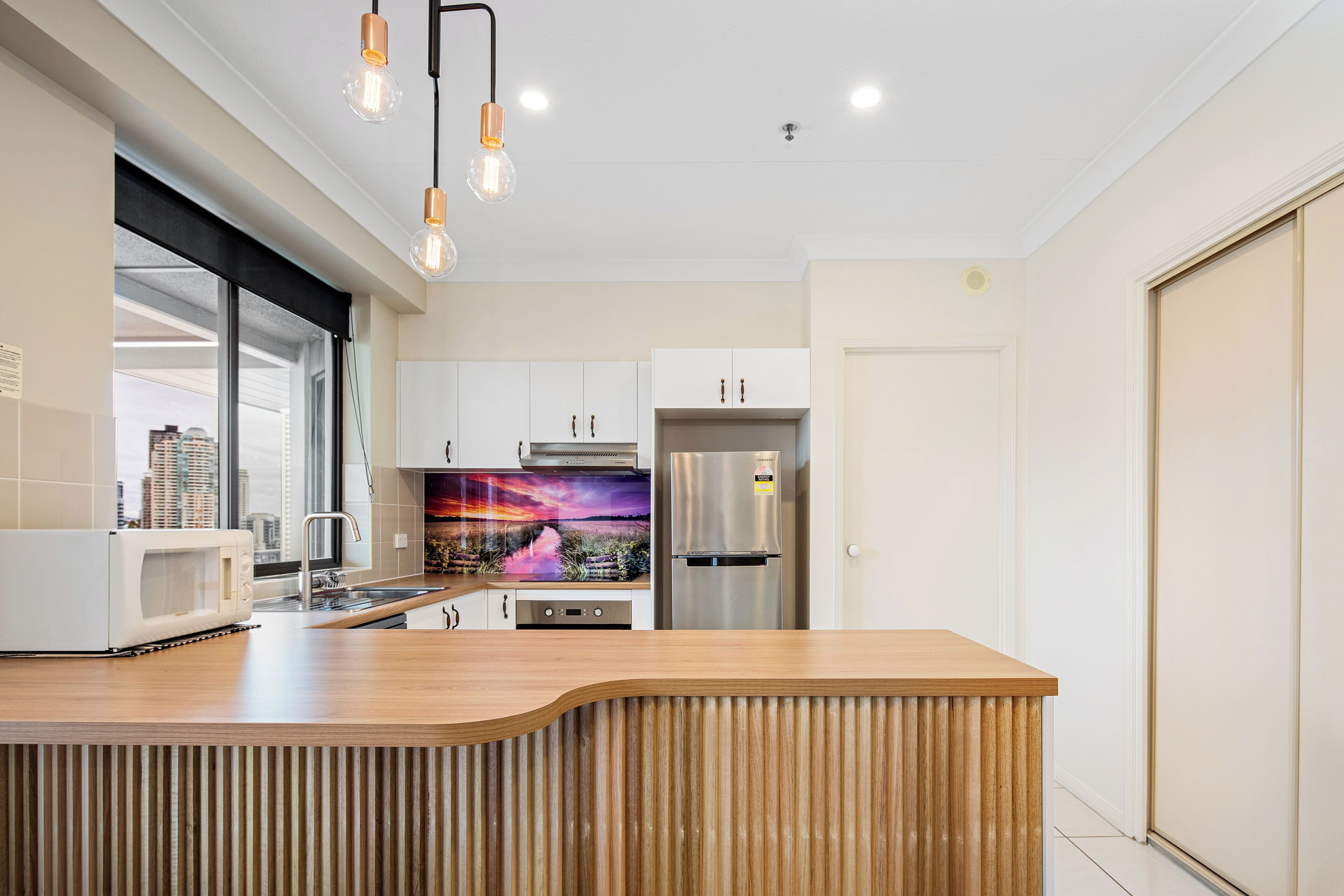 Une cuisine moderne dotée d’un îlot central en bois, d’appareils électroménagers en acier inoxydable et de luminaires suspendus.