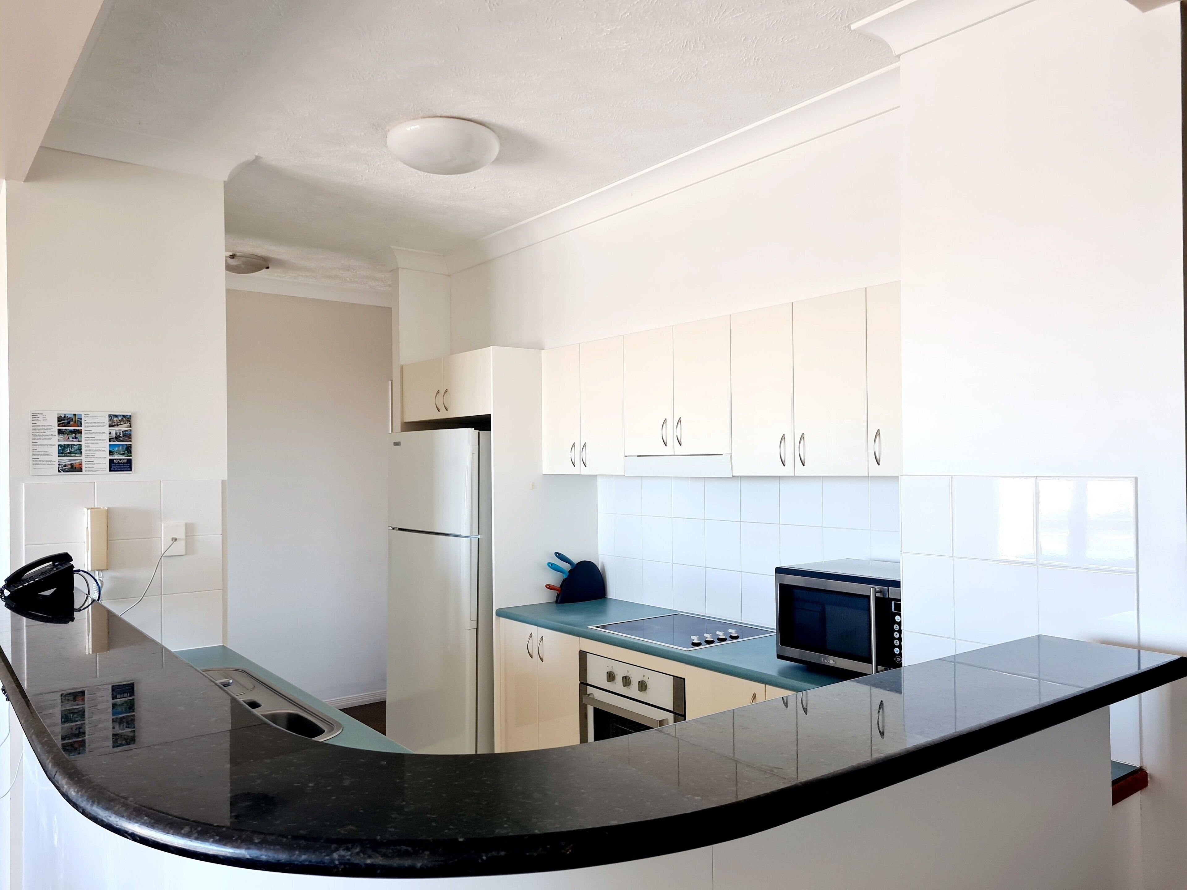 A modern kitchen with white cabinets, a black countertop, a refrigerator, a stove, and a microwave.