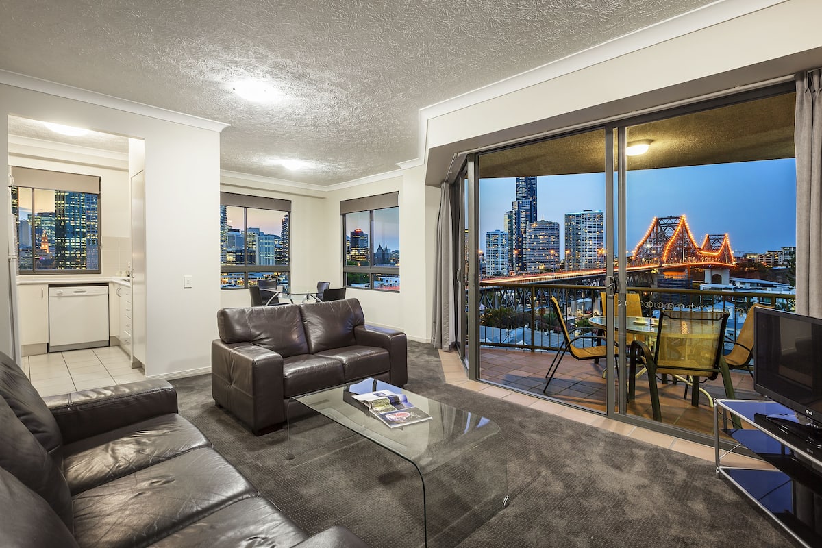 A modern living room with a glass coffee table, leather sofa, and a city view through large windows.