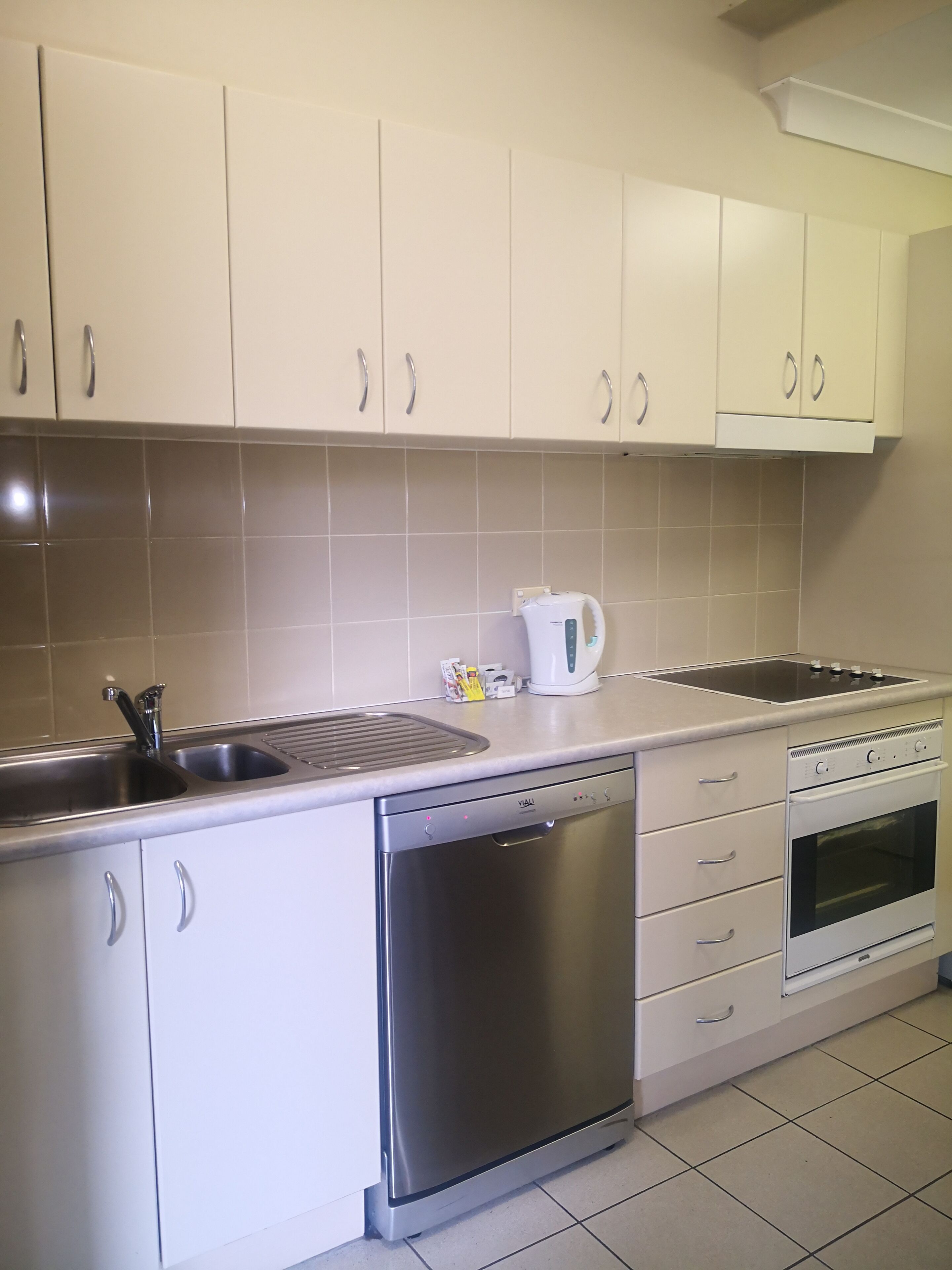 Een moderne keuken met witte kastjes, roestvrijstalen apparatuur en een betegelde spatwand.