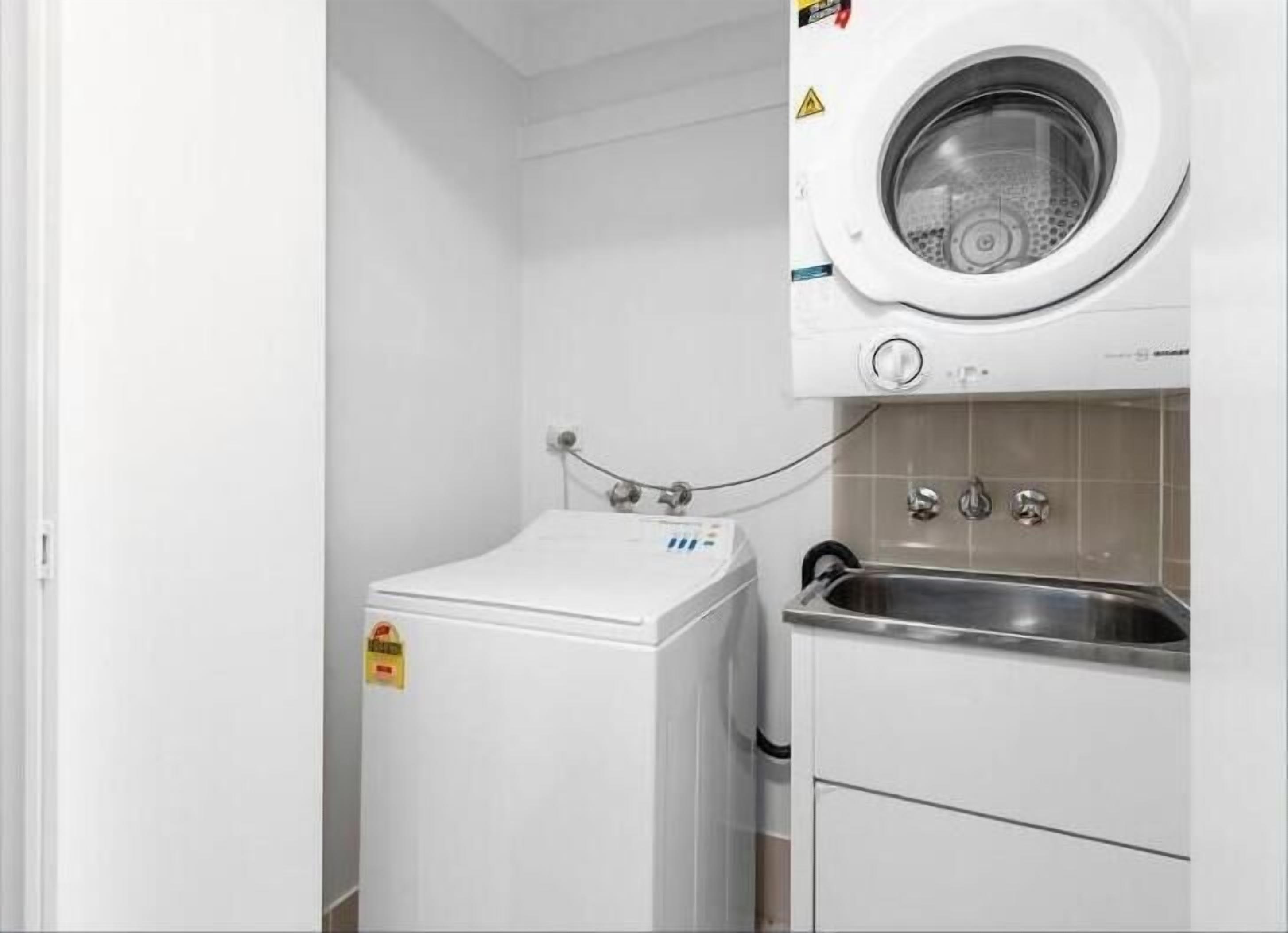 A compact laundry room with a front-loading washing machine, a small dryer, and a sink.